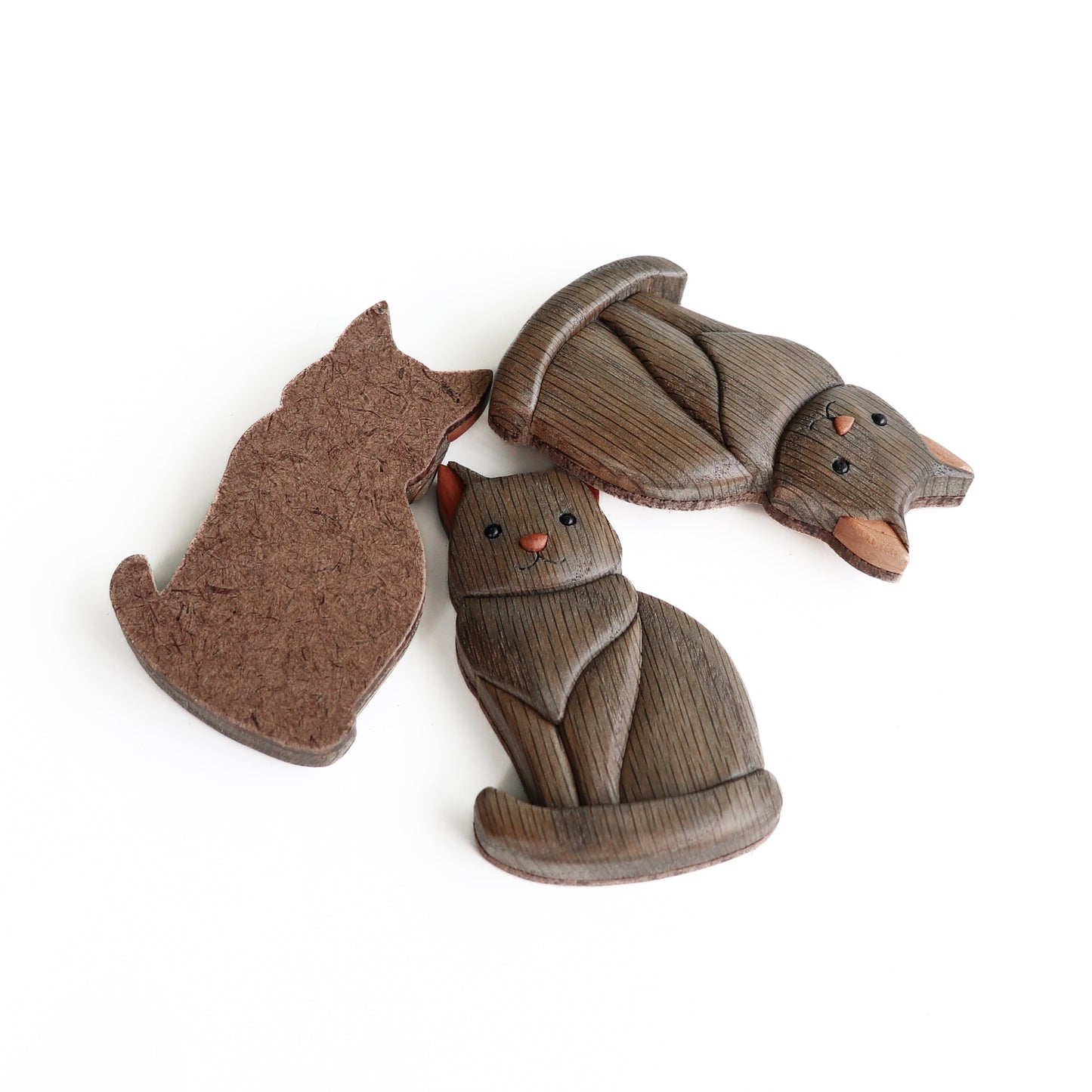Three gray wooden cats made from ebonized oak with red cedar ears made using the style of woodworking called intarsia and a hardboard backing ready for including a magnet or a screw eye for a ornament string.