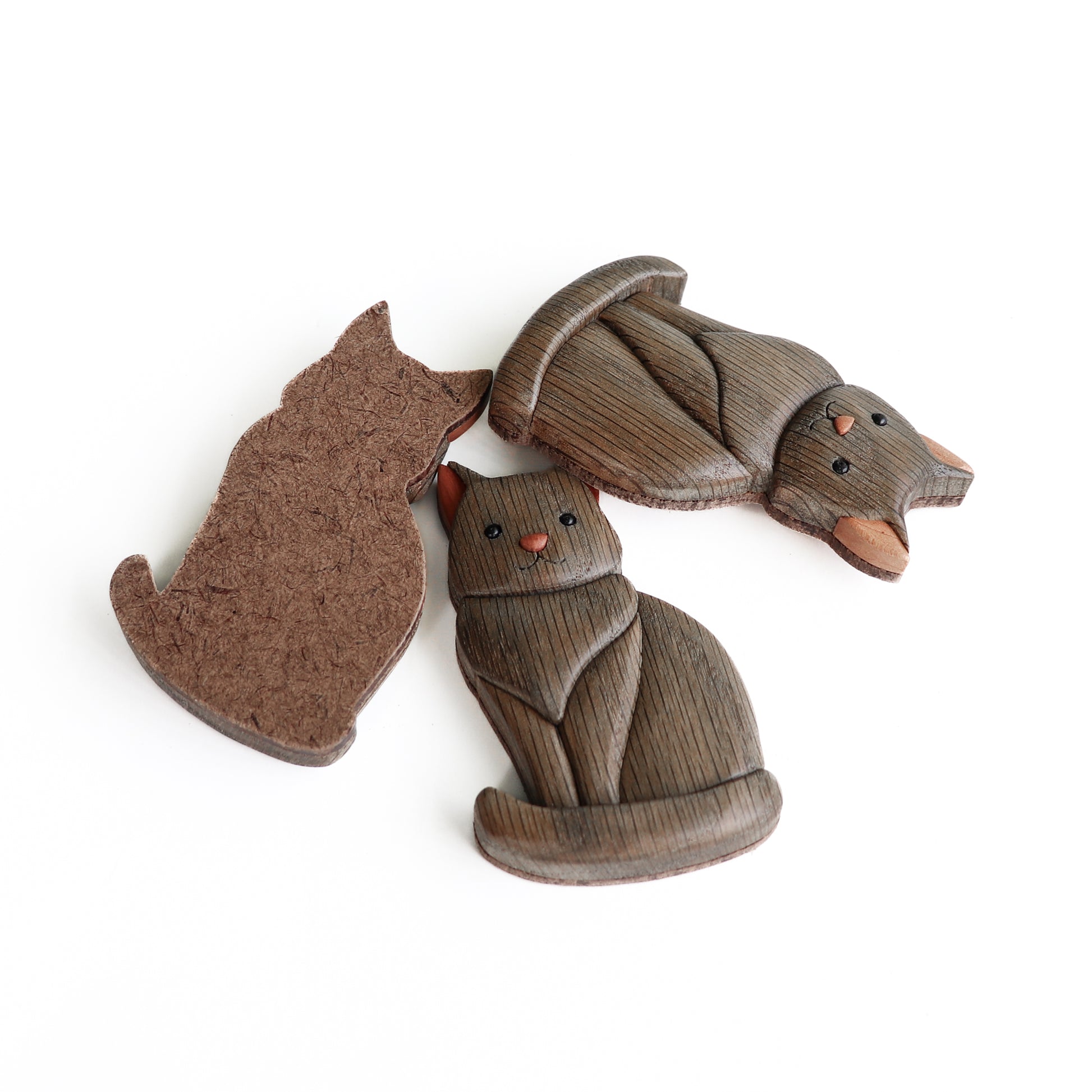 Three gray wooden cats made from ebonized oak with red cedar ears made using the style of woodworking called intarsia and a hardboard backing ready for including a magnet or a screw eye for a ornament string.