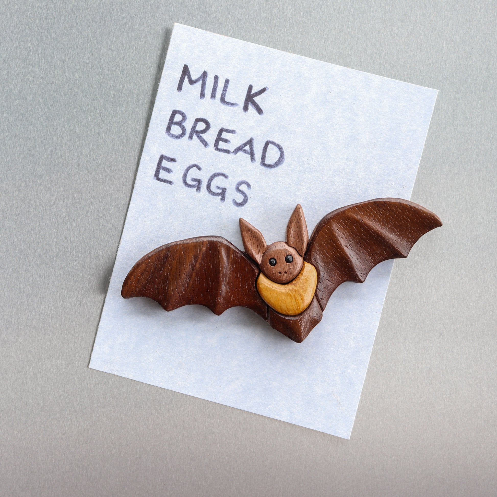 bat magnet holding up a piece of paper that has grocery list on a silver refridgerator.