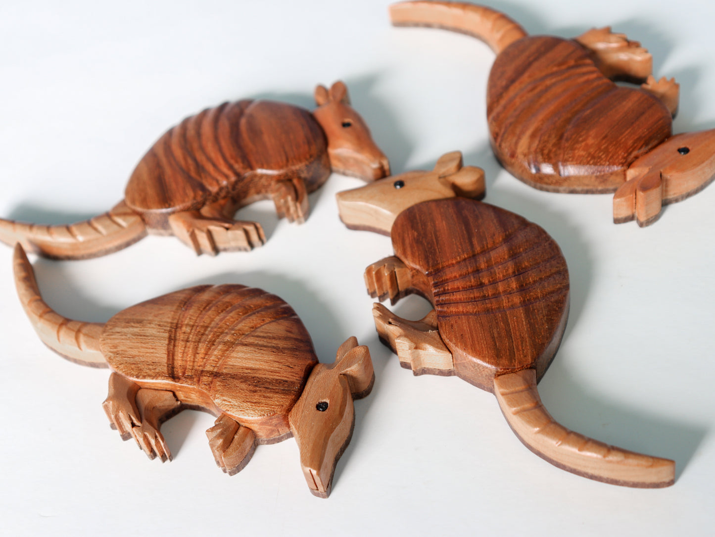 four wood armadillo carving using the intarsia style technique woodworking, all laying down showing flat backs laying on a white background.