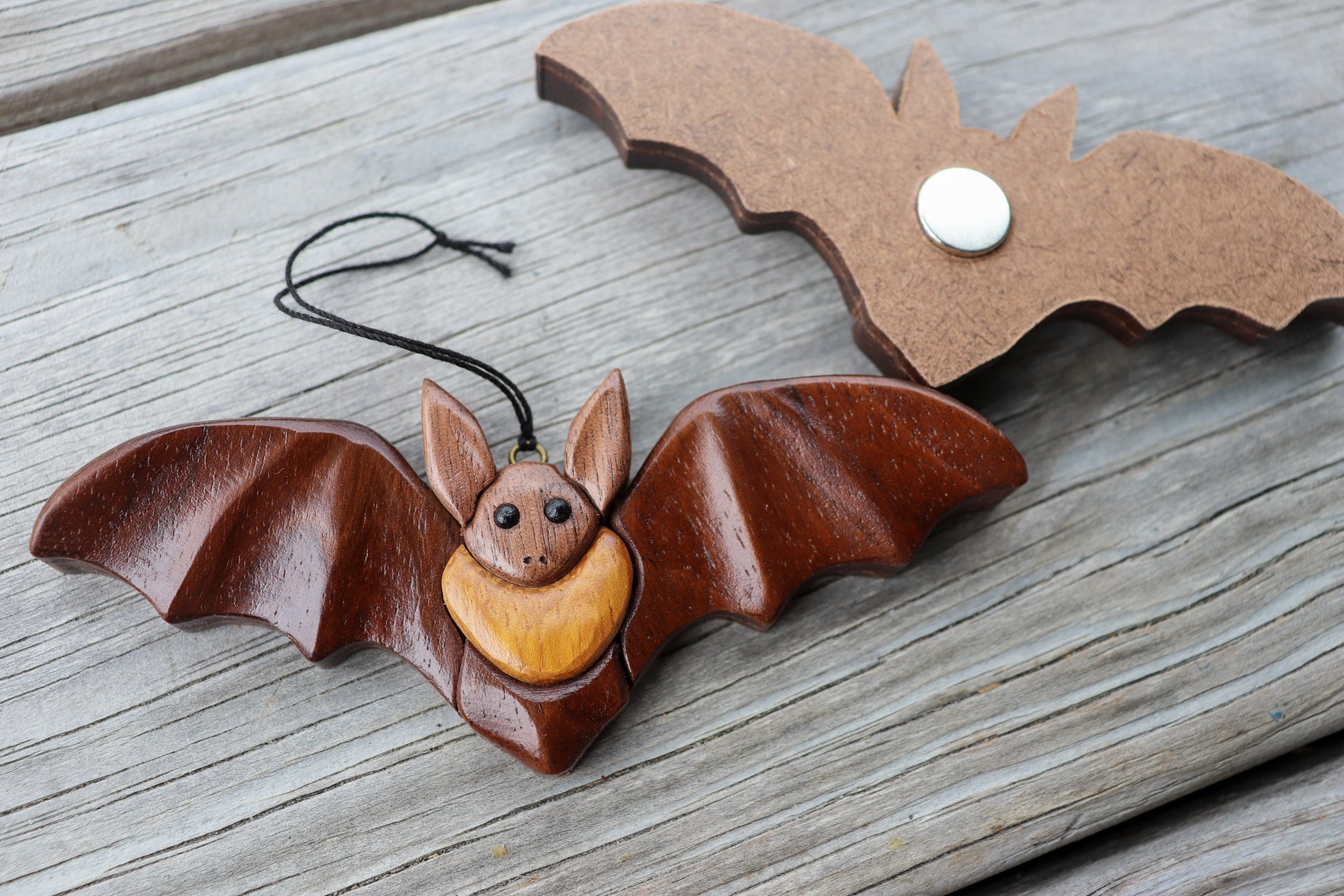 zoomed up image of a two bats, one showcasing an ornament with a screw eye and a string, and the other flipped over showing the hardboard backing and a neodymium magnet inset in the back.