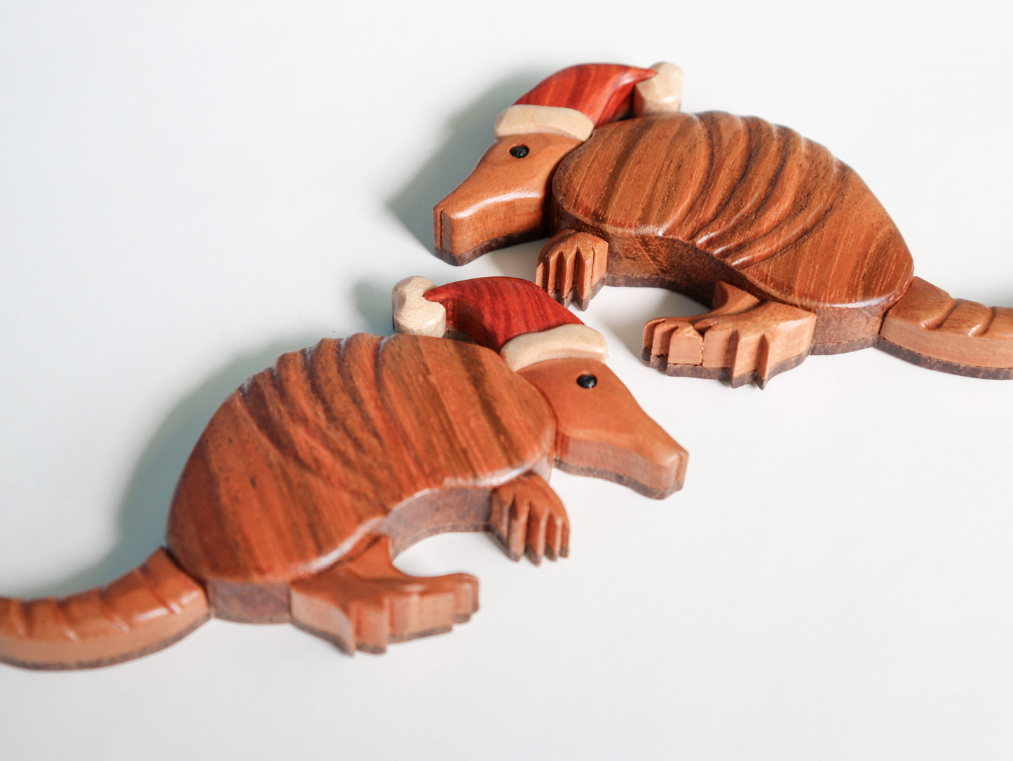 two wooden armadillo wearing santa hats laying down showcasing the flat backs and the carved detail of their shell along with the brazilian cherry woodgrain.