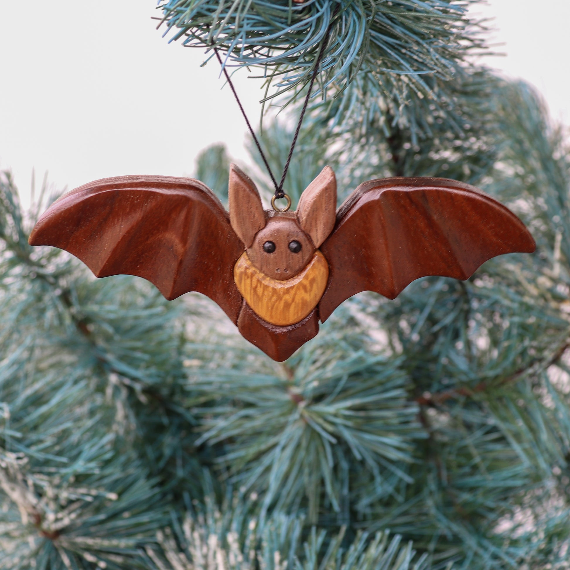 walnut bat and iroko ornament wood carving with a screw eye and a string hanging on a christmas tree.