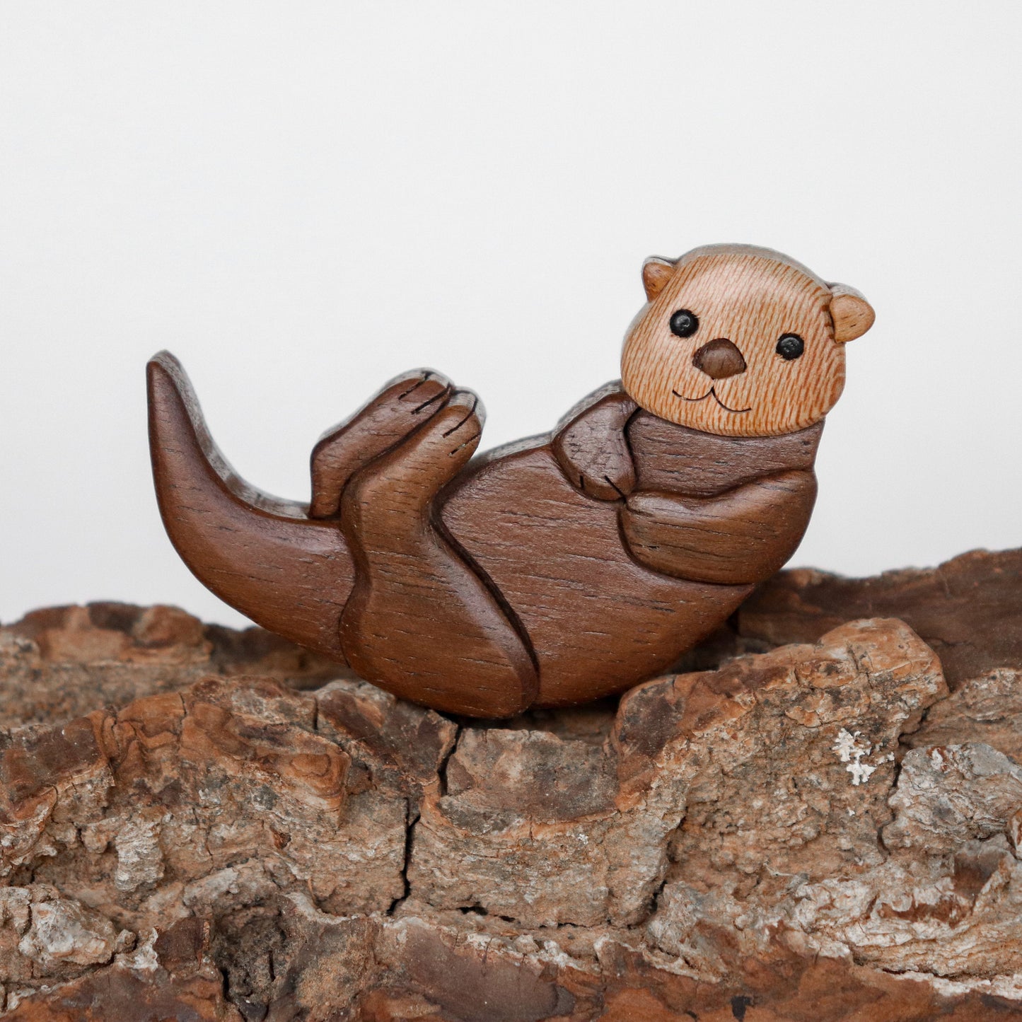 Wood carving style of intarsia of a sea otter laying on its back, made from peruvian walnut, and sycamore.