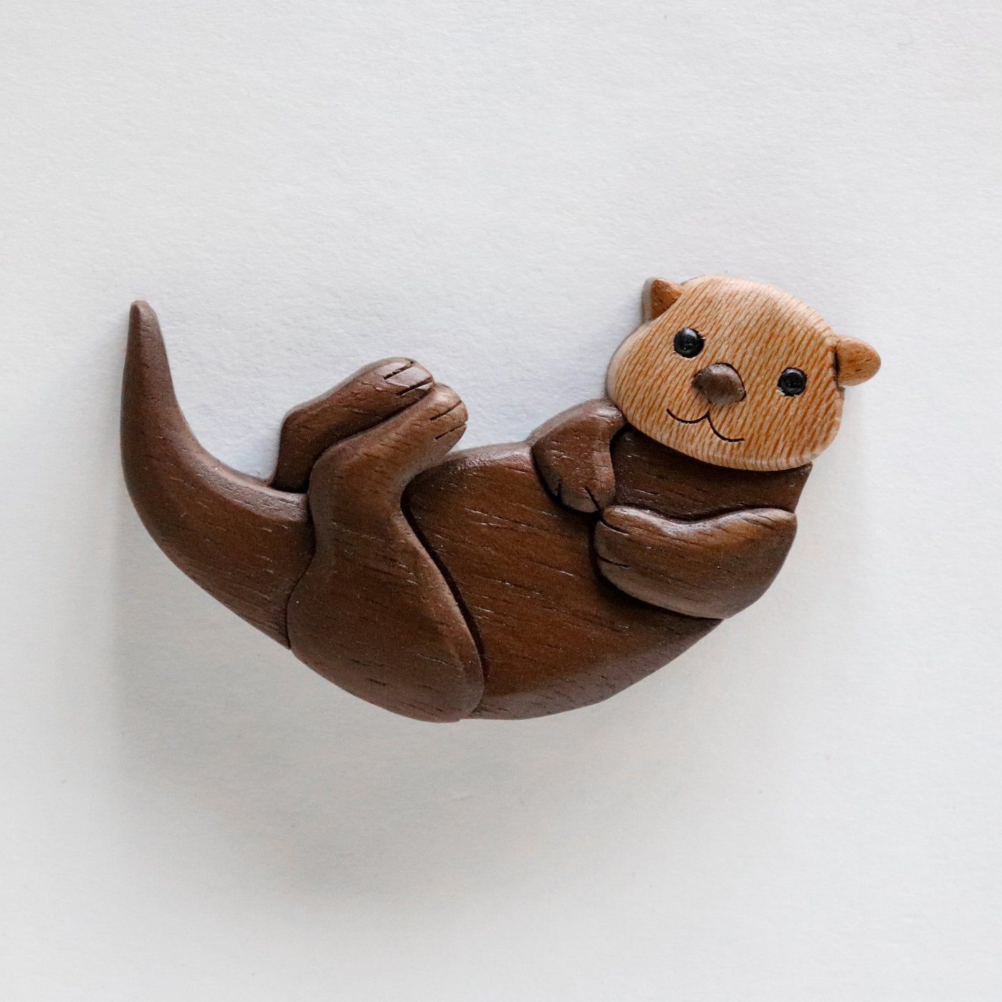 Single sea otter miniature wood intarsia , made from natural colors of wood, laying on a white background.