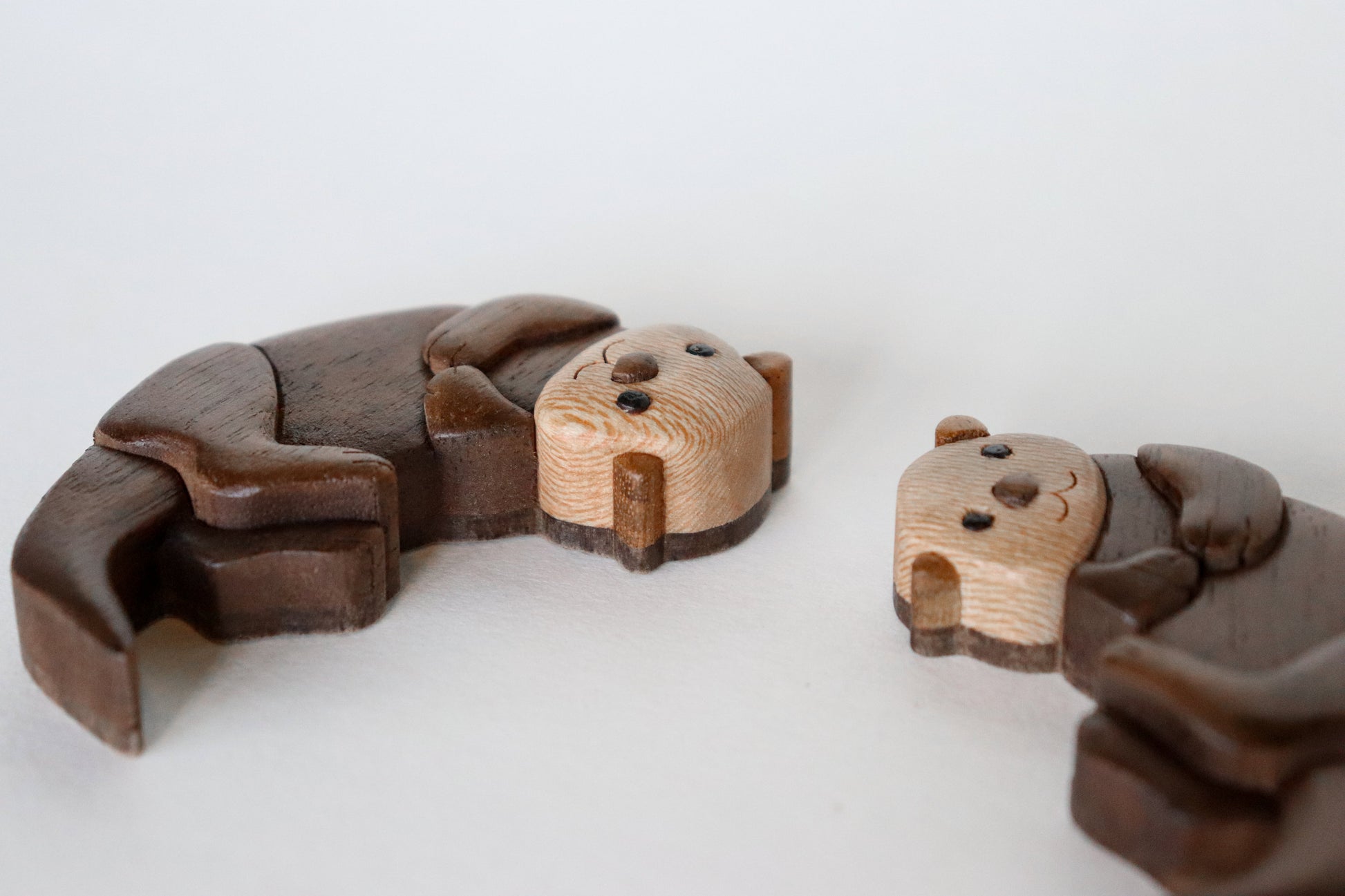 Two wooden sea otter intarsia miniature laying on their side showcasing the flat backs and the sycamore woodgrain.