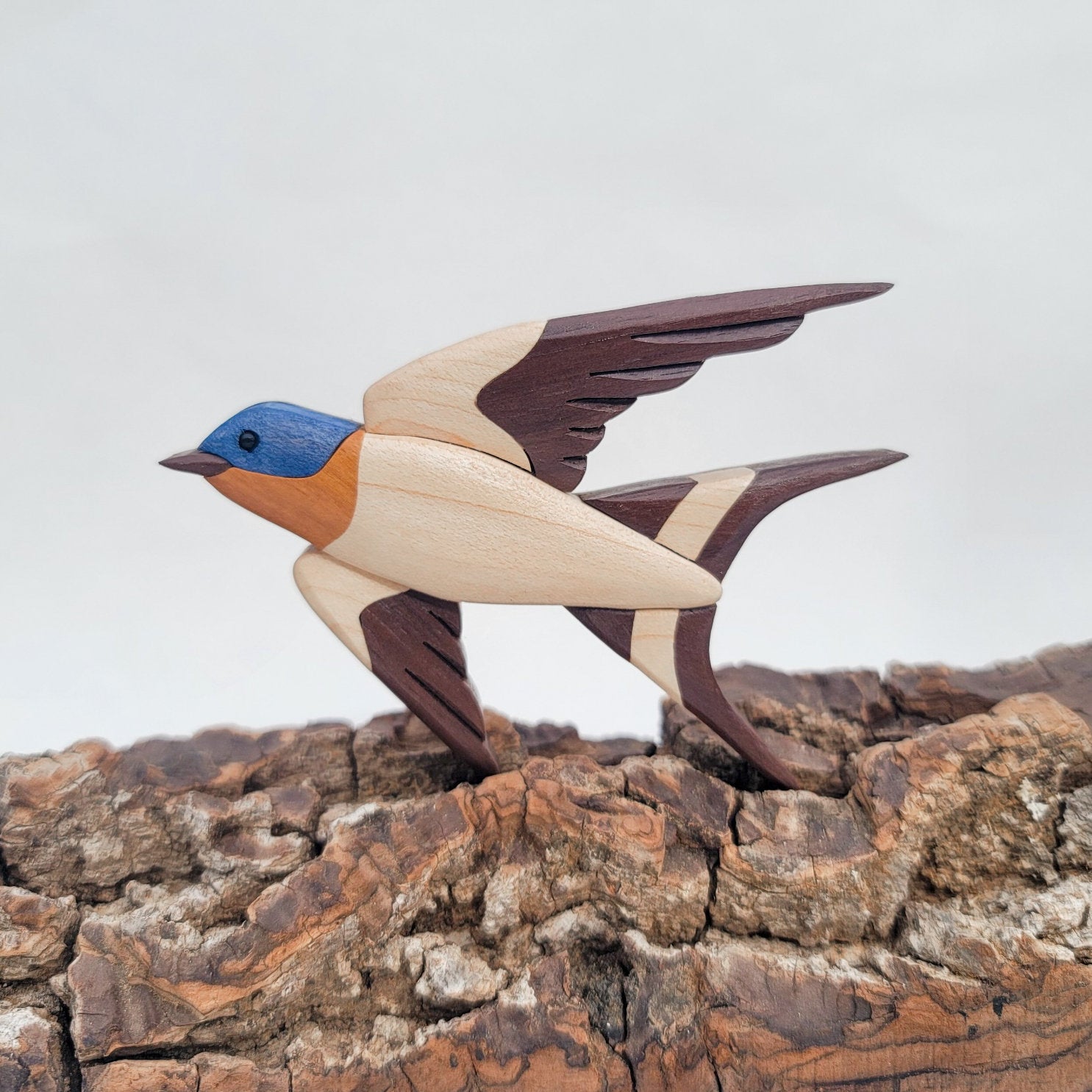 miniature wood intarsia of a barn swallow in flight facing left, made from the woods chakte viga, maple, peruvian walnut. showing inlays and cuts done by a scroll saw