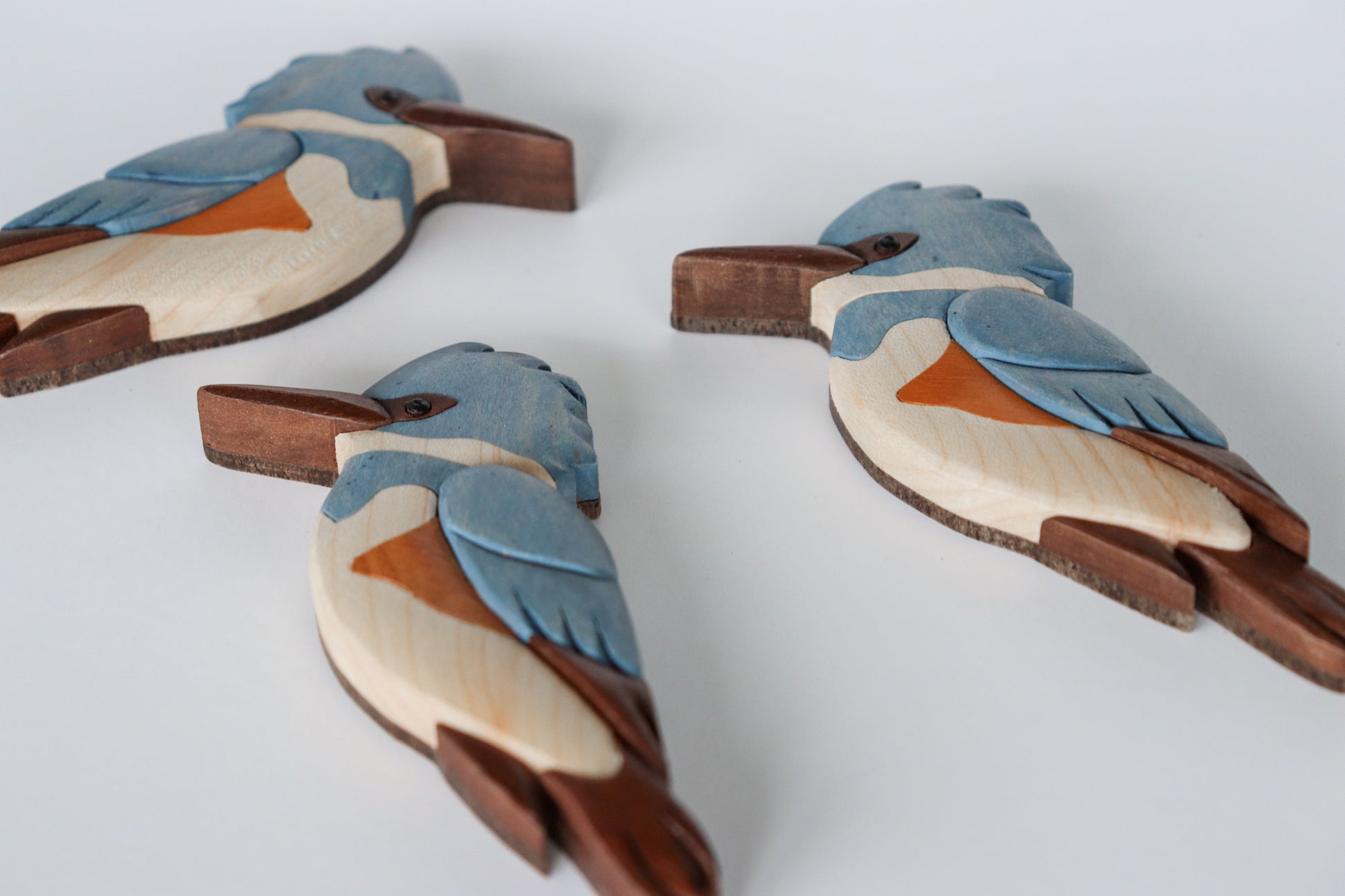 Three wood carved kingfishers laying on the back, showing the flat backside of the carving with a hardboard backing material.