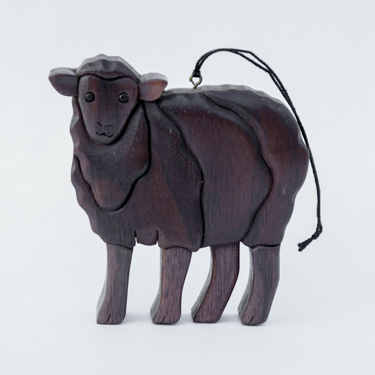 wood carved black sheep with black wool made from peruvian walnut, with a screw eye and string attached to its back ready for hanging on a tree.