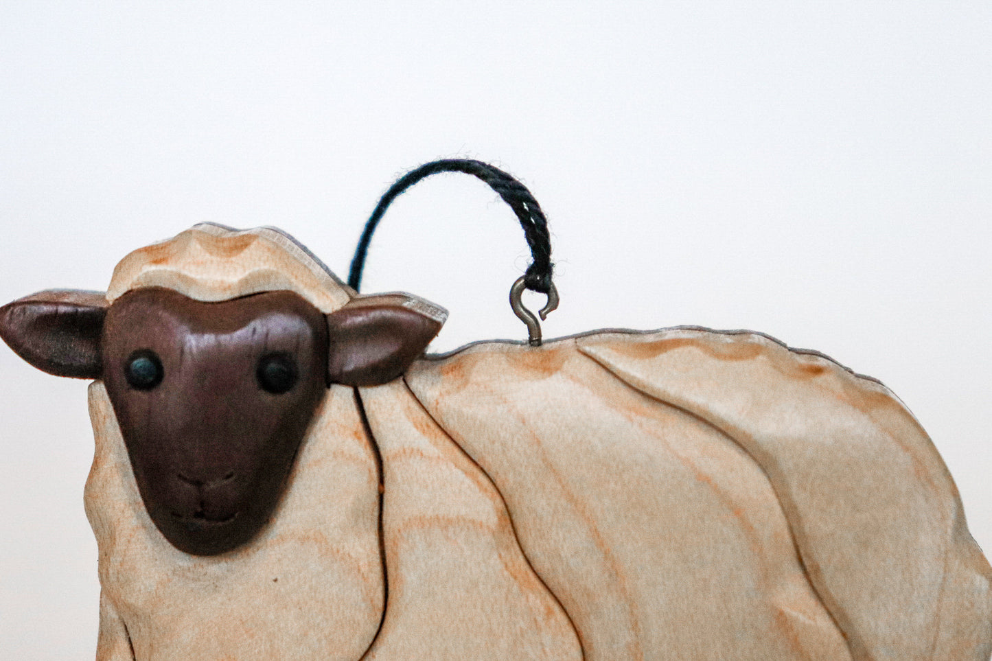 close up of a screw eye with a string attached to it on a white sheep wooden christmas ornament.