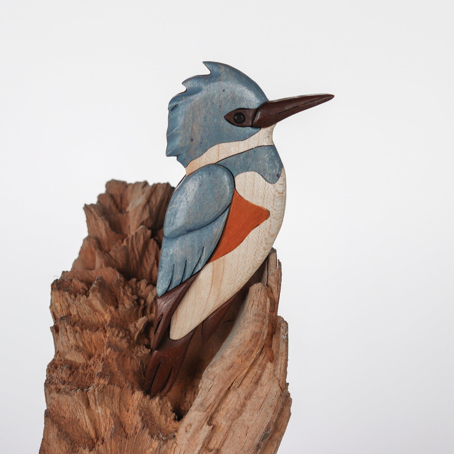 zoomed up power wood carved and hand cut kingfisher facing right with a long beak and tufted head feathers.