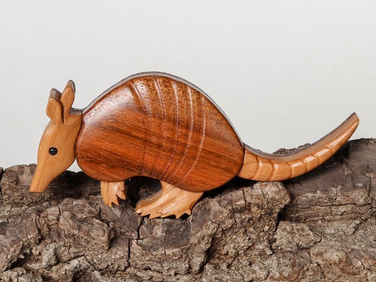 wood carved armadillo cut with a use of a scroll saw made from Brazilian cherry, and american cherry standing on a bark prop with white background.