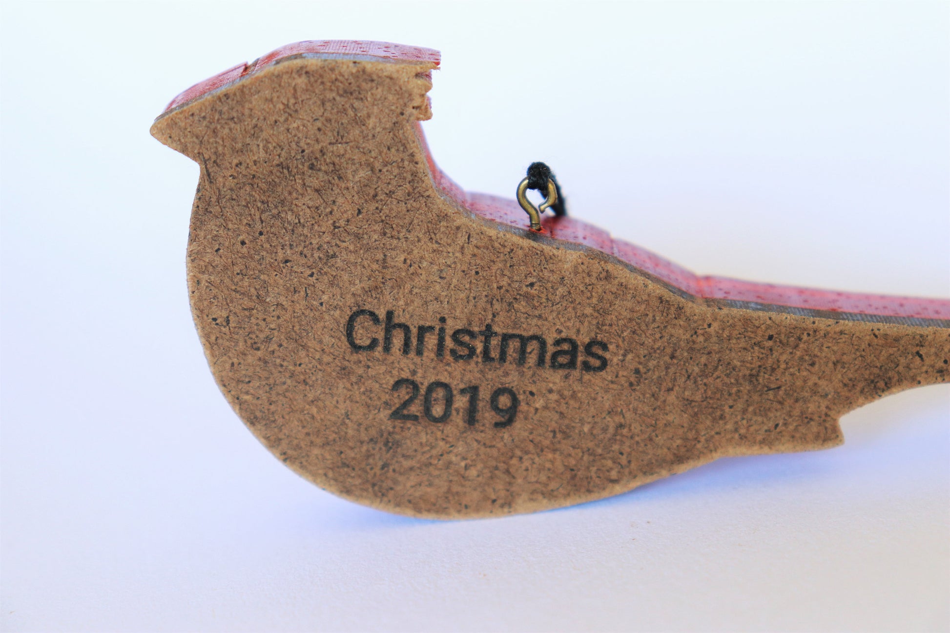 example of a laser burned personalization on the hardboard backing material of the wood carved cardinal ornament personalized with the words, "Christmas 2019" and attacked to the top of the ornament is a screw eye and string.